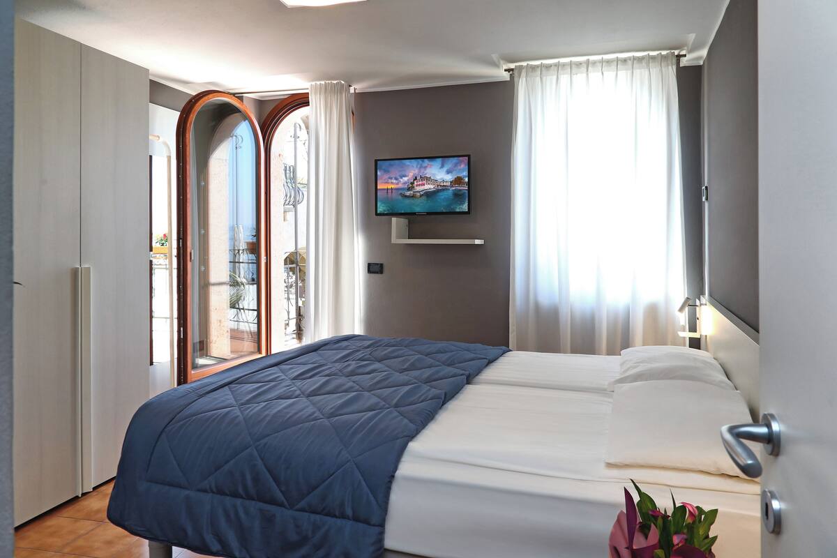 Quarto de hotel com cama, televisão fixada na parede e vista para o exterior através de uma porta.