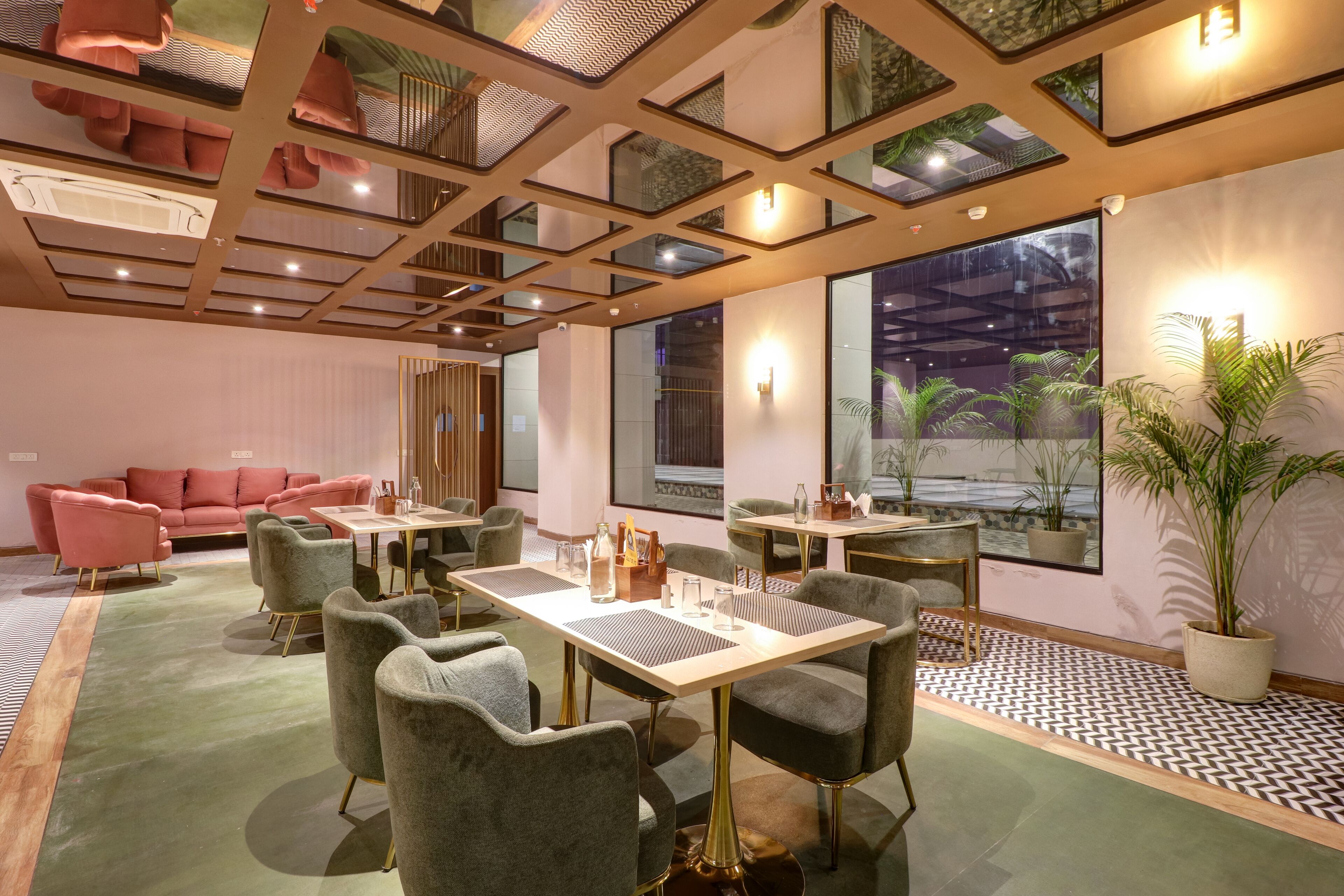 Un intérieur moderne avec une moquette verte, des fauteuils à revêtement gris et un canapé rose. Des tables sont dressées avec de la verrerie et une bouteille.