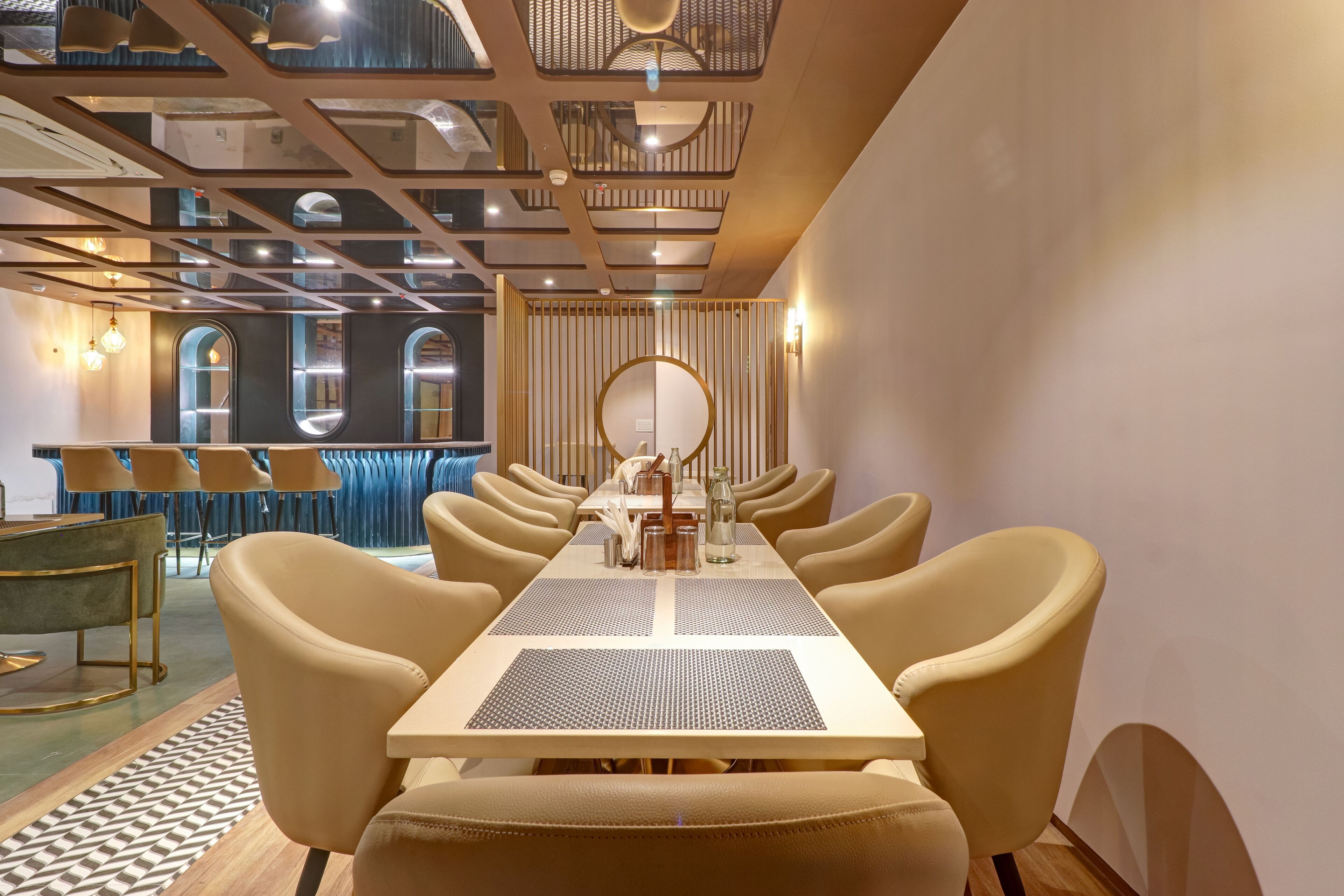 A modern hotel dining area with a long table, beige chairs, and a decorative mirror.