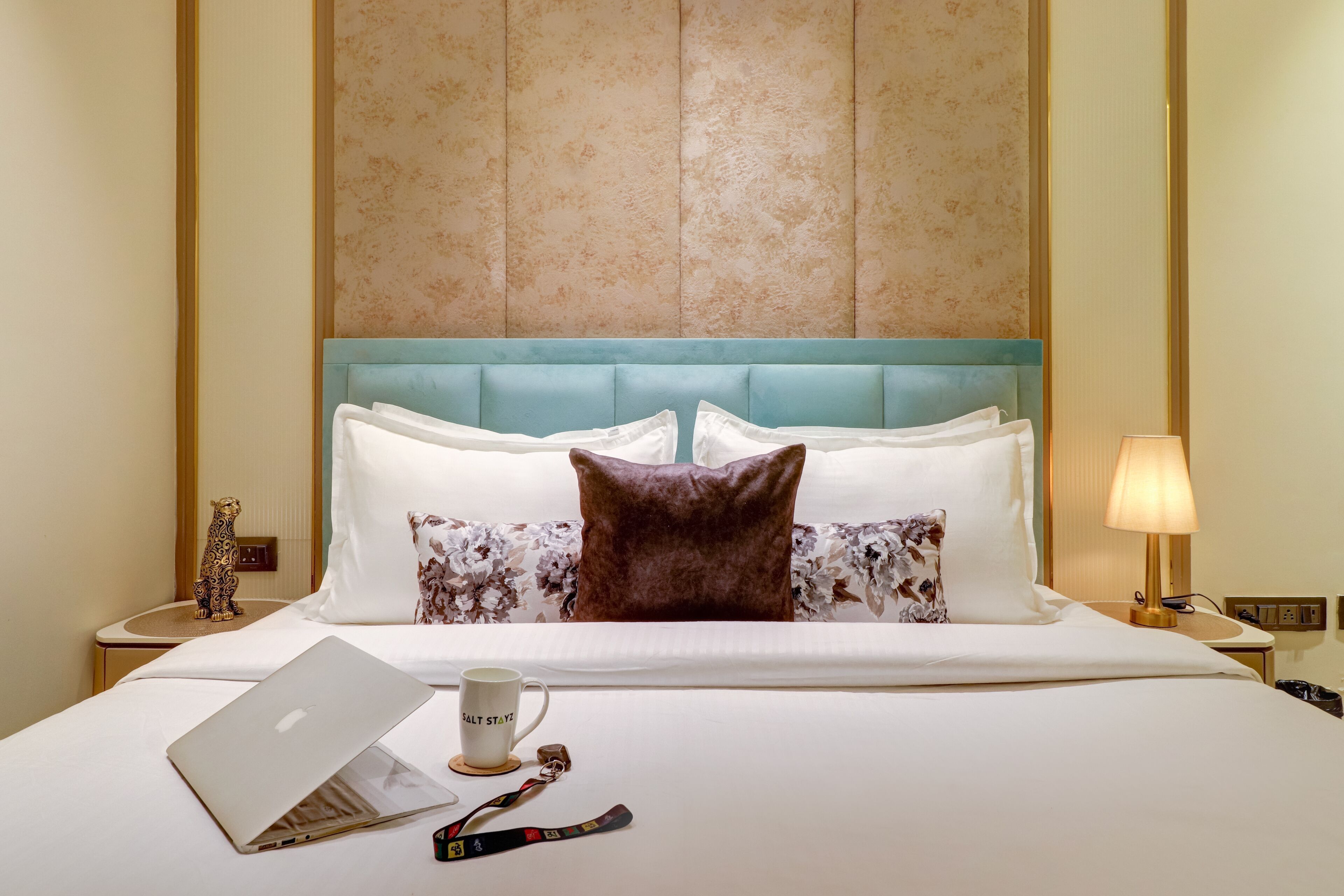 A neatly made bed with a laptop, a mug, and a keychain on the bedside table.