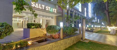 A hotel entrance with a sign reading "SALT STAYZ" and a well-lit pathway leading to the entrance.