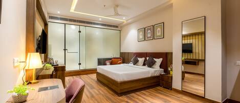 Une chambre d’hôtel moderne avec un plancher en bois, un lit doté d’une tête de lit en bois, un bureau avec une lampe, une chaise, une armoire et un miroir.
