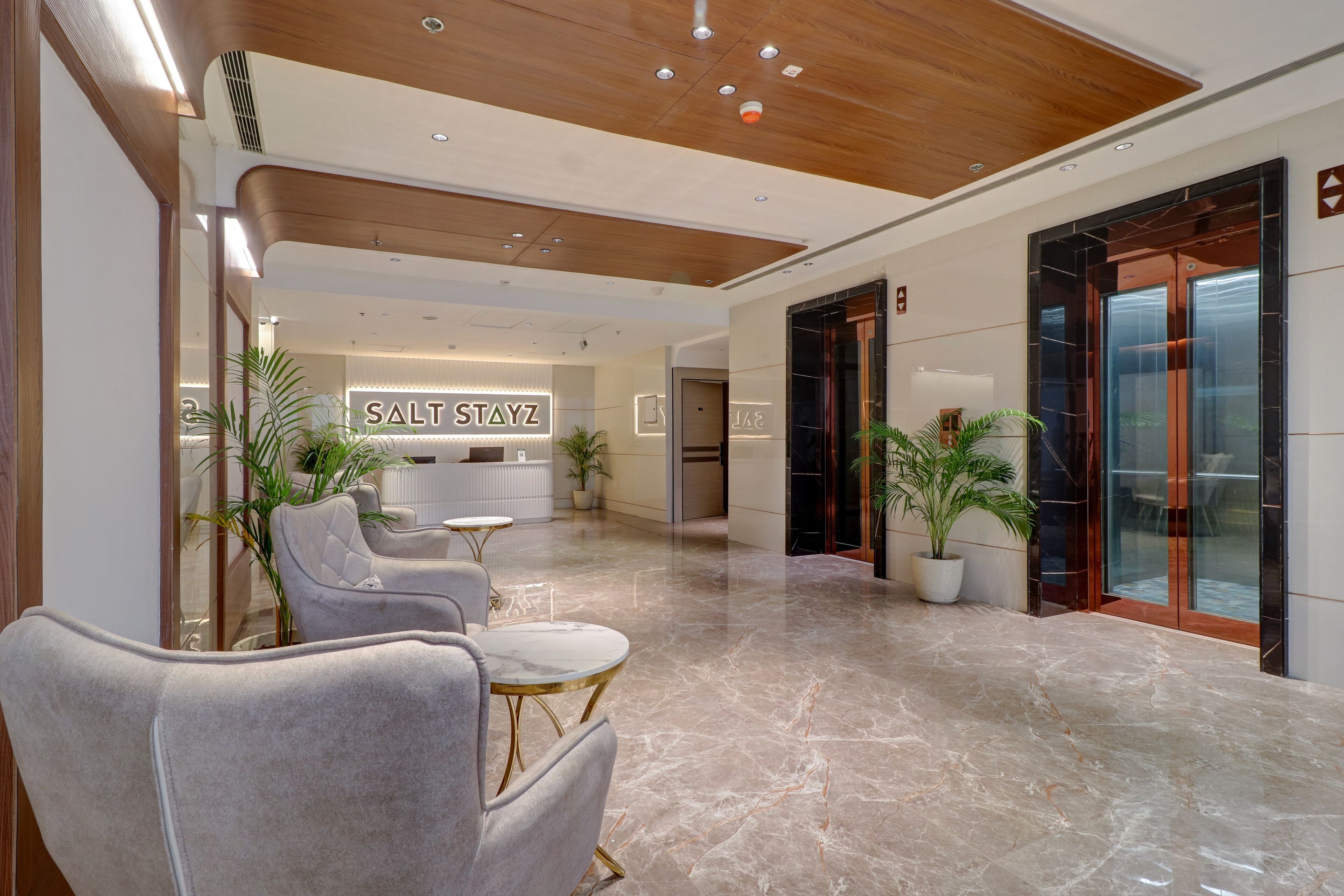 A modern lobby with marble flooring, a reception desk, and a seating area with armchairs and a small table.