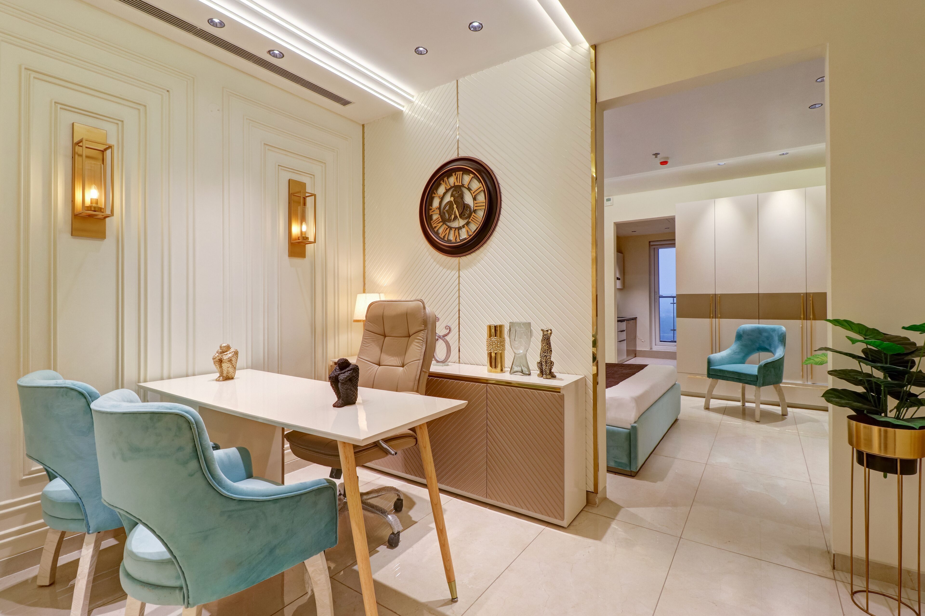 A modern dining area with a white table, blue chairs, a beige chair, and a decorative clock on the wall.