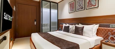 Una habitación de hotel moderna con una cama grande, un televisor y una puerta corrediza a un balcón.