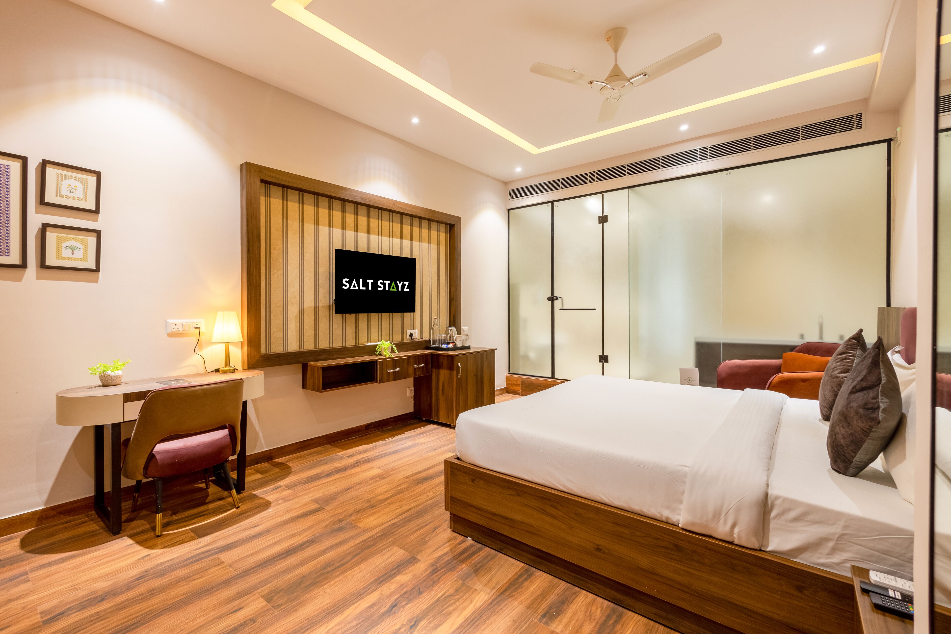 Ein modernes Hotelzimmer mit Bett, Schreibtisch, Fernseher und einer Glastür, die auf einen Balkon führt.