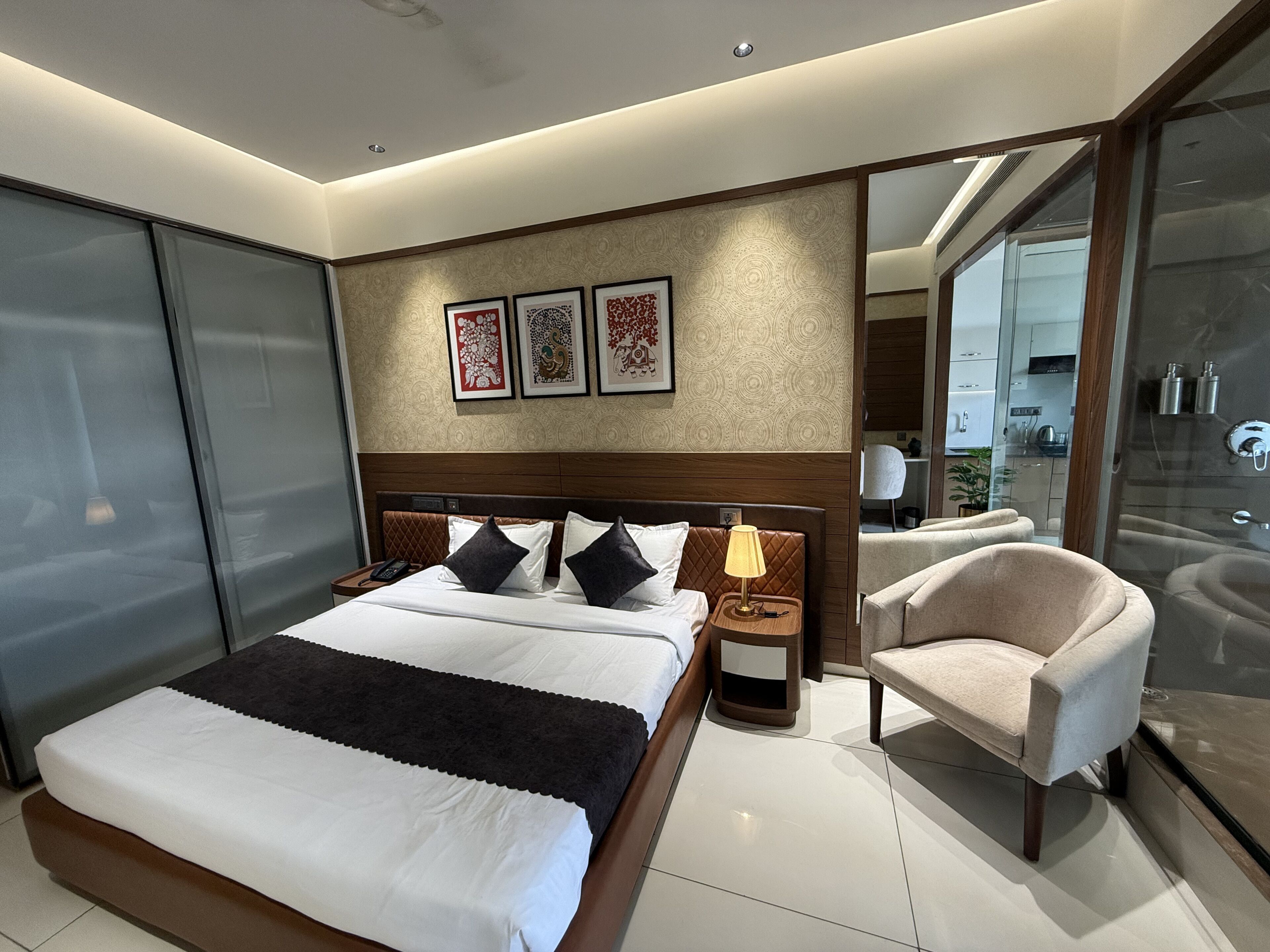 Een moderne hotelkamer met een groot bed, nachtkastje, stoel en glazen scheidingswand.