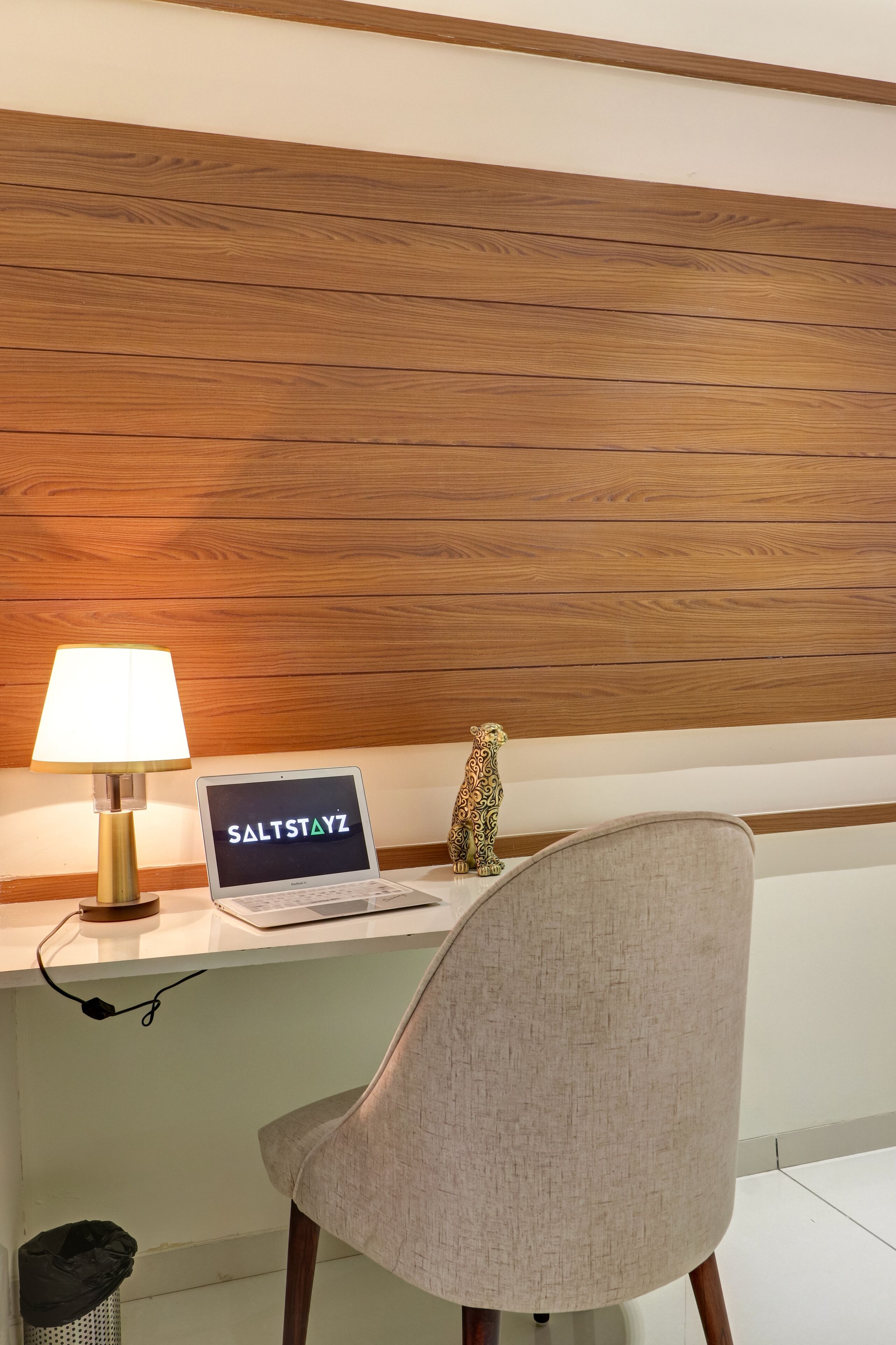 A hotel desk with a laptop displaying "SALTSTAYZ", a lamp, and a decorative animal figurine.