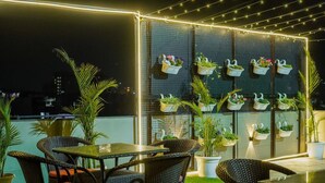 Une terrasse sur le toit, aménagée avec des meubles en osier, une table en verre et des plantes en pot.