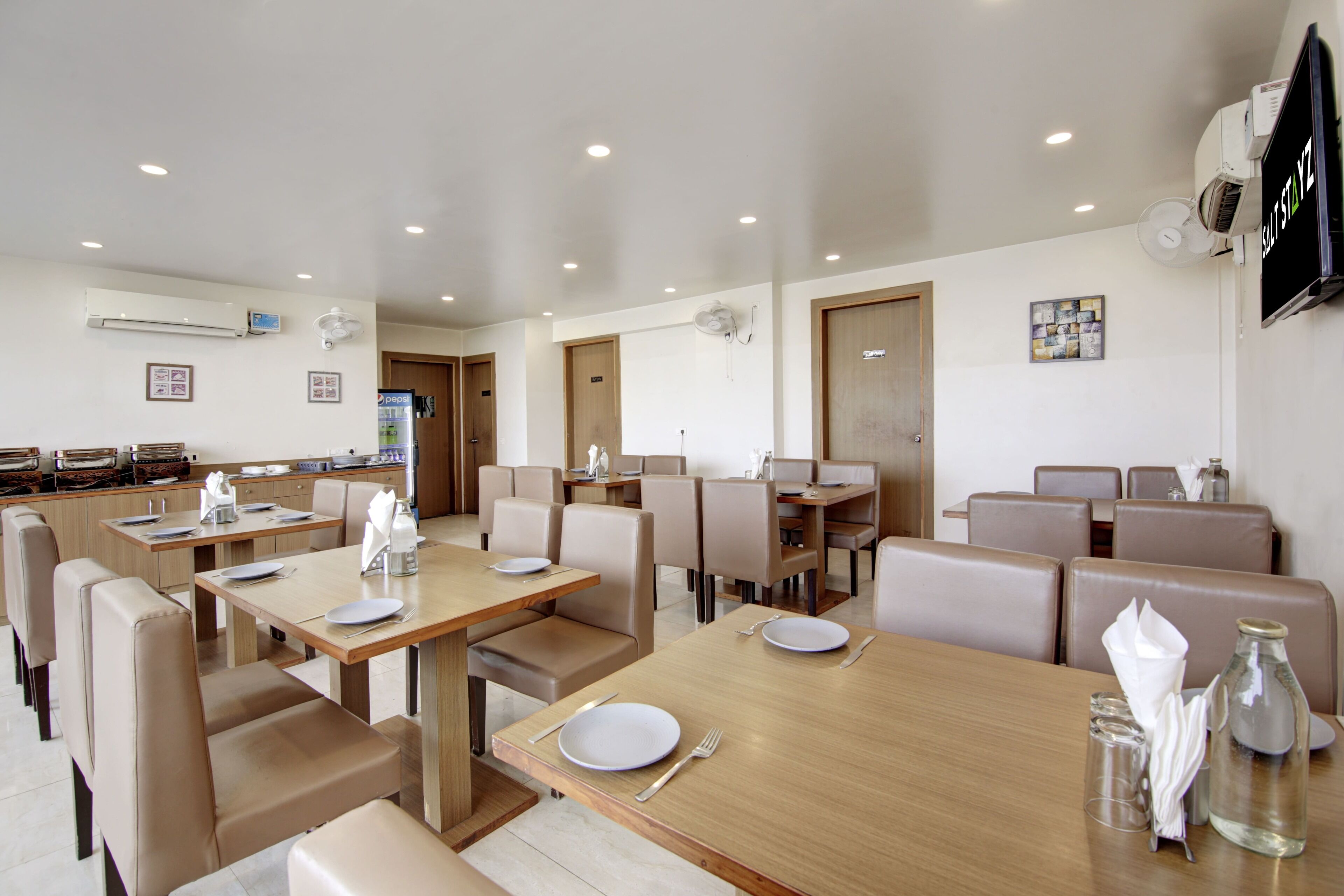 Un comedor moderno con varias mesas y cabinas, unidades de aire acondicionado y un televisor montado en la pared.