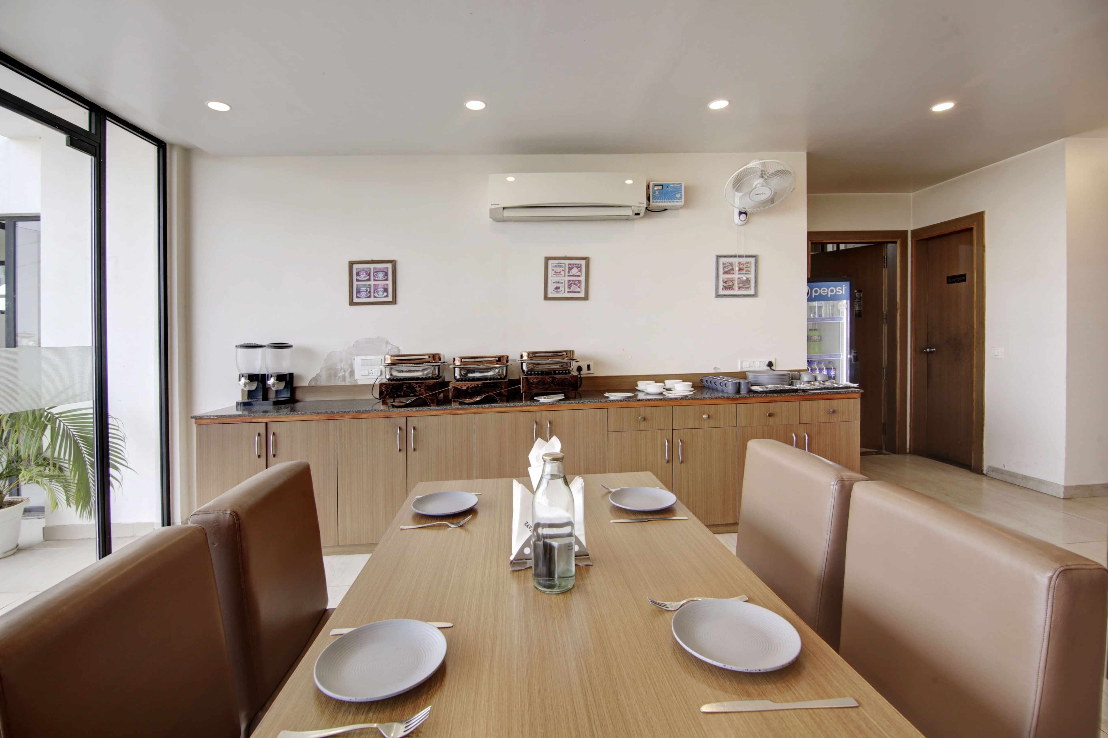 A dining area with a long table, brown cushioned booths, and a kitchen in the background.