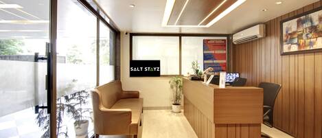 A modern reception area with a wooden reception desk, a sofa, and a potted plant.
