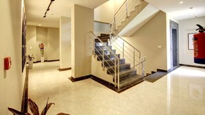 A modern interior with a staircase, a fire extinguisher, and a hallway with a plant. - Saltstayz Select - Golf Course Road & Sector 27 (Gurugram)