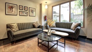 A modern living room with two grey sofas, a glass coffee table, and framed artwork on the wall. - Saltstayz Select - Golf Course Road & Sector 27 (Gurugram)