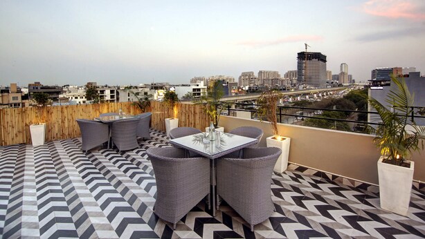 A rooftop terrace with a geometric patterned floor, a table with chairs, and potted plants. - Saltstayz Select - Golf Course Road & Sector 27 (Gurugram)