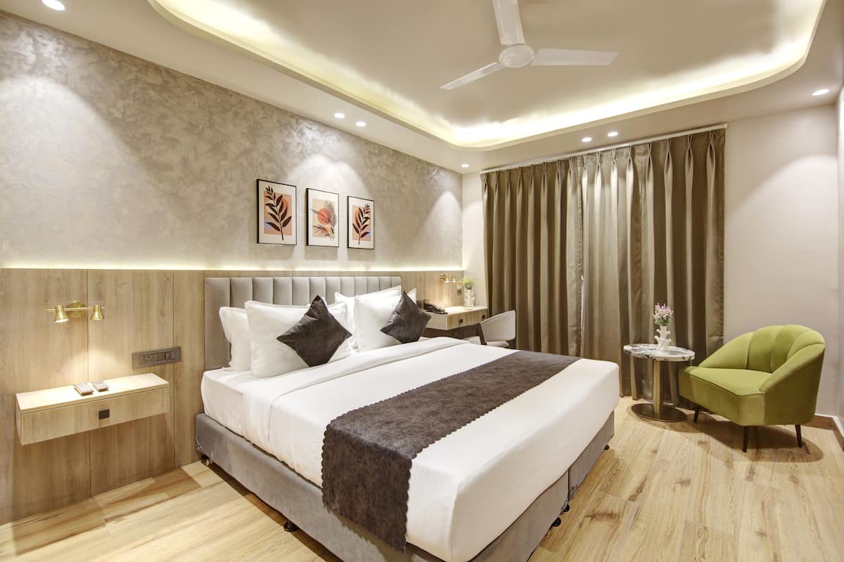 A modern bedroom with a large bed, bedside tables, a green armchair, and a ceiling fan.