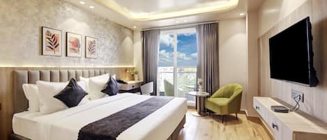 A modern hotel room with a large bed, a desk, a green armchair, and a flat-screen TV.