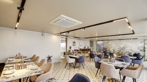 A dining area with tables set for two, chairs, and a kitchen in the background. - Saltstayz Premier - Near Golf Course Road & Sector 57 (Gurugram)