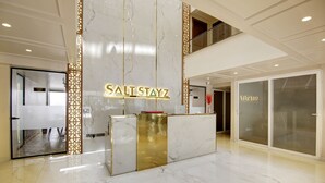 A reception desk with a marble finish and a gold accent, a glass door entrance, and a sign that reads "SALT STAYZ". - Saltstayz Premier - Near Golf Course Road & Sector 57 (Gurugram)