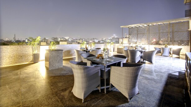 An outdoor patio area with a dining table and chairs, potted plants, and a cityscape view in the background. - Saltstayz Premier - Near Golf Course Road & Sector 57 (Gurugram)