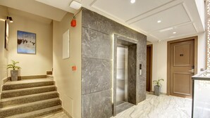 A modern hotel lobby with a marble staircase, an elevator, and a painting on the wall. - Saltstayz Premier - Near Golf Course Road & Sector 57 (Gurugram)