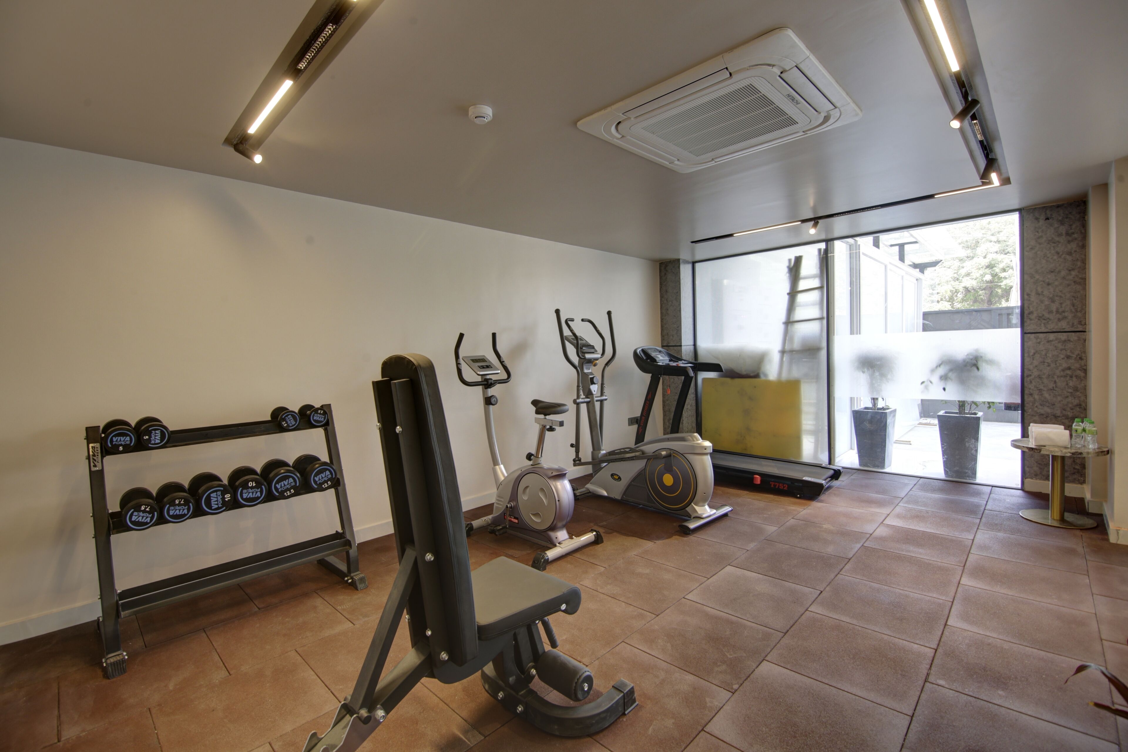 Un gimnasio con equipo de ejercicio, un soporte para pesas y un ventanal grande.