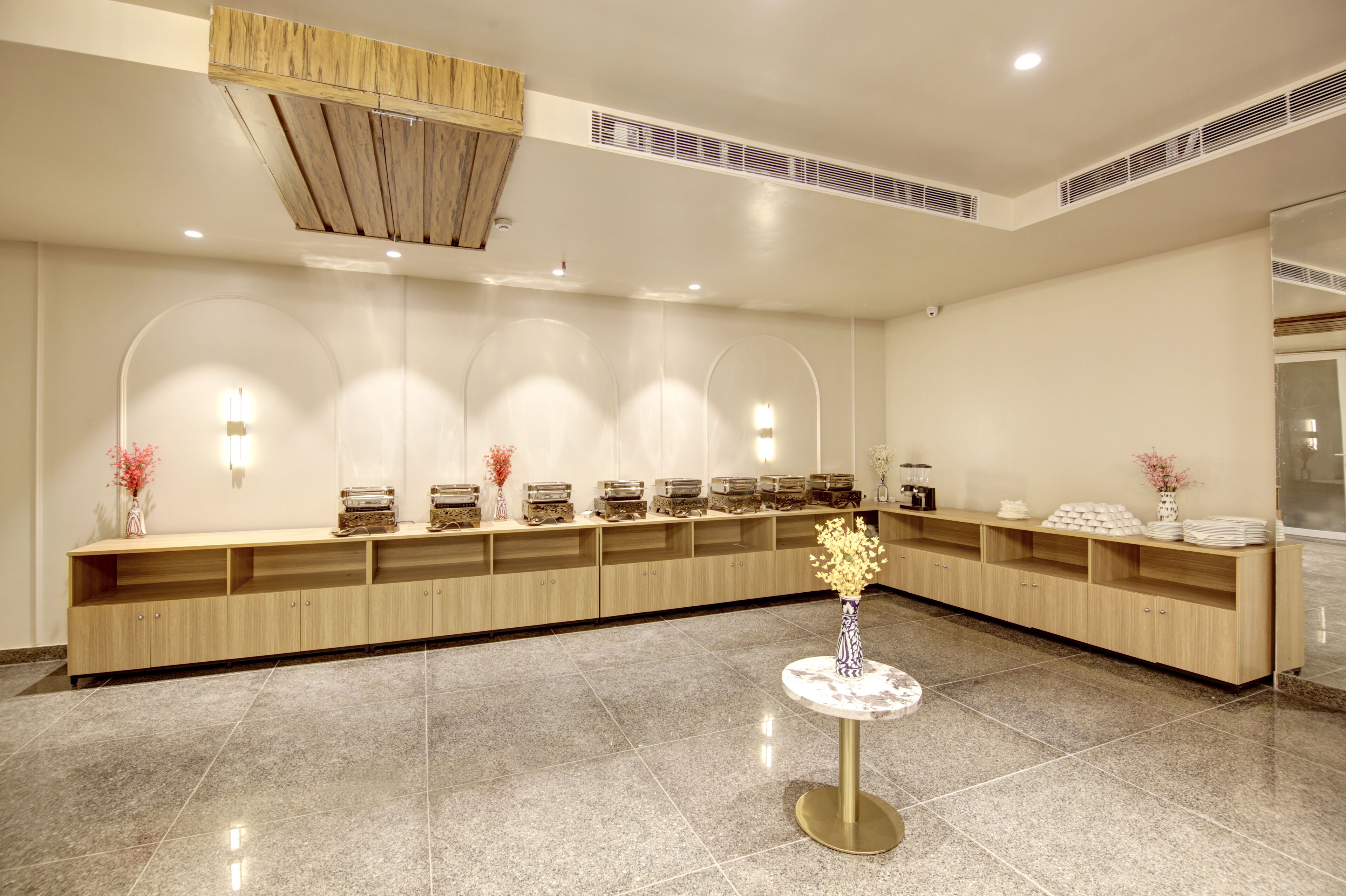 A reception area with a long wooden counter, a round table with a vase, and wall-mounted lighting.
