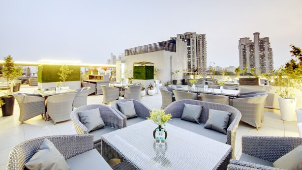 Una terraza en la azotea con mesas al aire libre, una zona de bar y vistas a edificios altos.