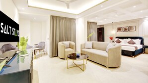 Una habitación de hotel moderna con sofá, sillones, una mesa de centro, cama y escritorio con computadora.