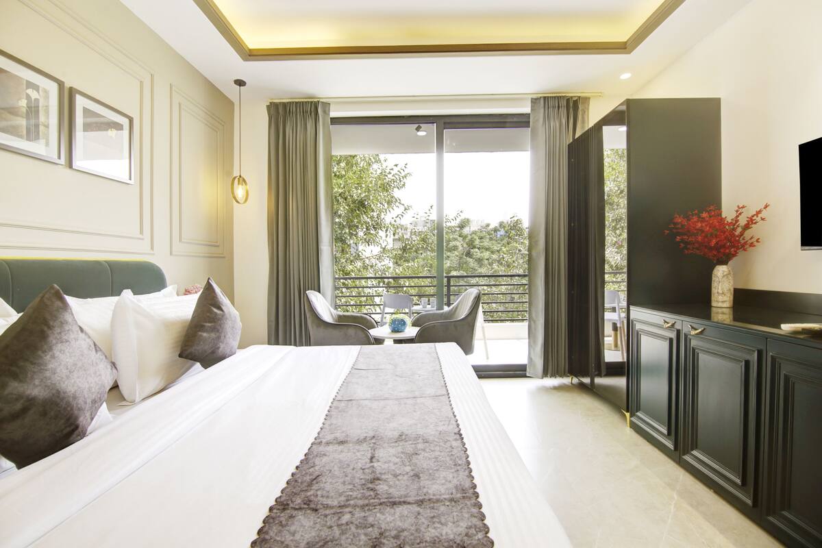 Ein Hotelzimmer mit einem großen Bett, einem Essbereich mit Stühlen, Blick durch eine Schiebetür und einem an der Wand befestigten Fernseher.