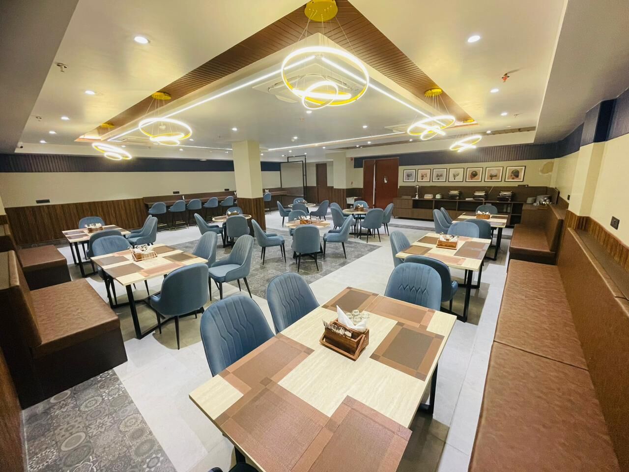 A spacious dining area with multiple tables and chairs, a modern ceiling design, and a neutral color palette.