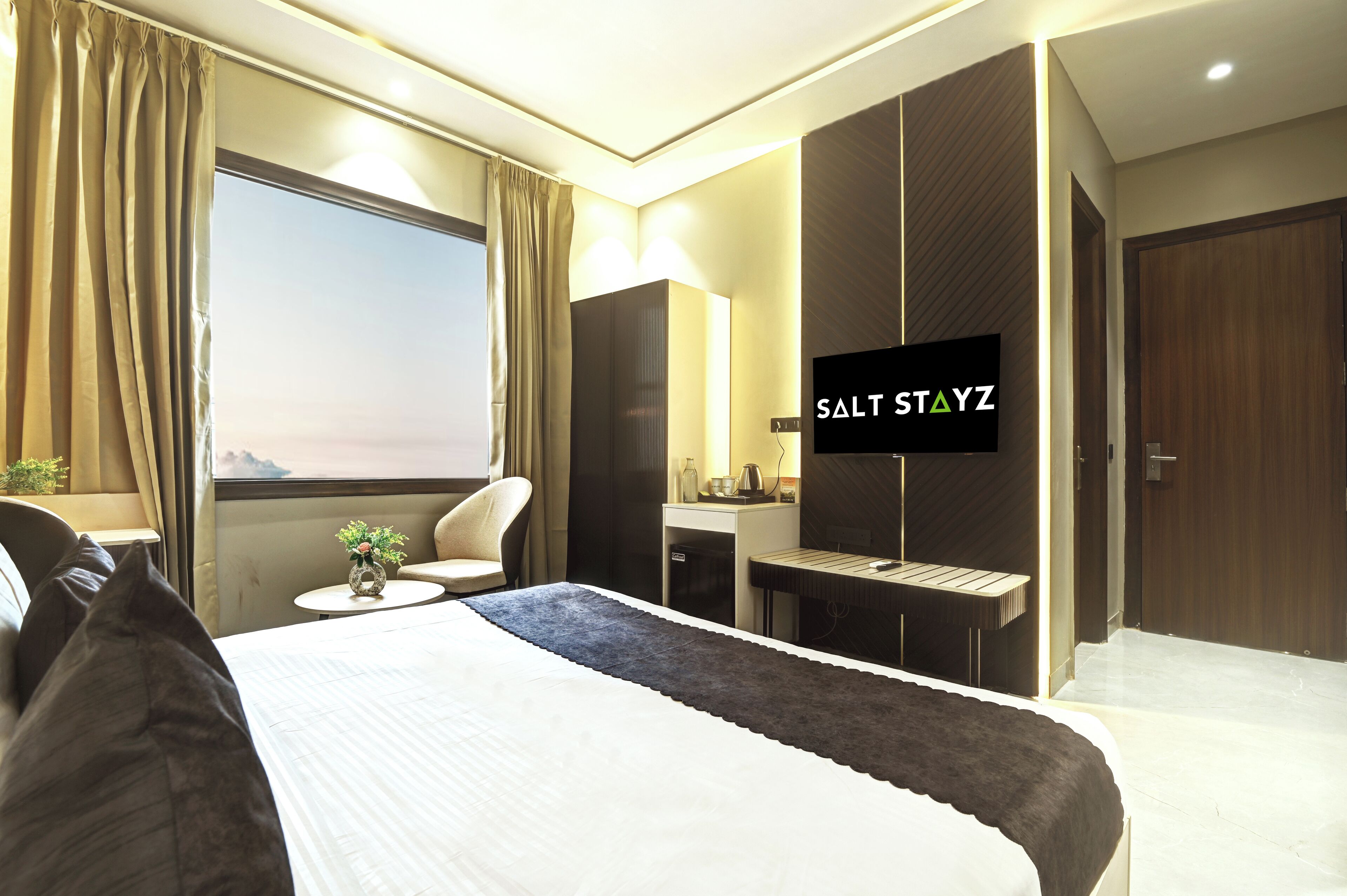 Ein modernes Hotelzimmer mit einem großen Bett, einem Schreibtisch, einem Sessel, einem Fernseher und Blick auf die Berge.