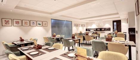 A modern dining area with multiple tables, chairs, and a kitchen in the background.