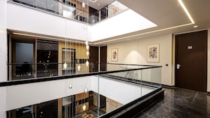 A modern hotel interior with a glass railing, a mezzanine level, and artwork on the walls. - Saltstayz Premier – Golf Course Road & Sector 42 (Gurugram)