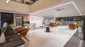 A modern hotel lobby with a reception desk, seating area, and a glass wall with a view. - Saltstayz Premier – Golf Course Road & Sector 42 (Gurugram)