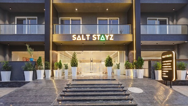 The entrance of Salt Stayz hotel with a modern design, featuring a glass facade, a staircase leading to the entrance, and potted plants around the area. - Saltstayz Premier – Golf Course Road & Sector 42 (Gurugram)