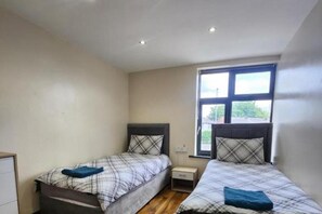 Ein kleiner, gut beleuchteter Raum mit zwei Betten, jeweils mit Kopfstütze und Kissen. Ein Fenster sorgt für natürliches Licht, und dazwischen steht ein kleiner Nachttisch.