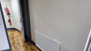 Un pasillo con suelo de madera, un bote de basura gris, un radiador blanco y un extintor en la pared.