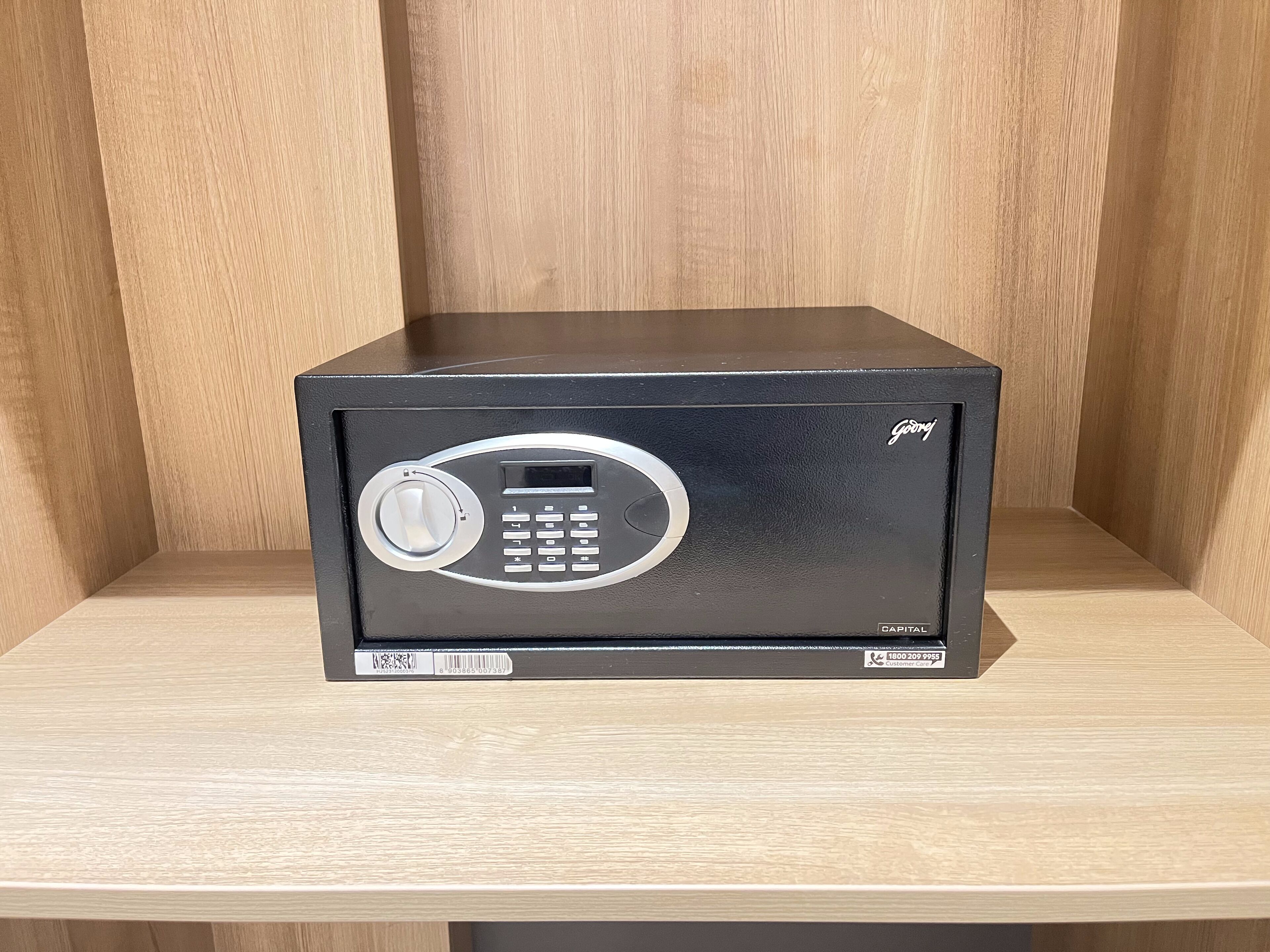 A black safe with a keypad and a dial lock, labeled "Goji" and "Capital," on a wooden shelf.