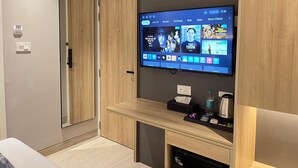 A hotel room with a mounted TV displaying various streaming options, a wooden cabinet, and a small table with a water bottle and other items. - AXON Bellandur by AXON Hotels (Bengaluru)