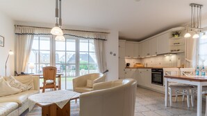Een moderne woonkamer met een bank, stoelen, een tafel en een keukenhoek met kasten en een fornuis.