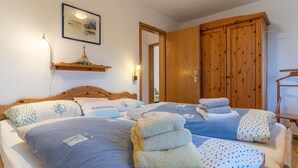 Een slaapkamer met twee bedden, een houten garderobe, een lijst met kunstwerk aan de muur en een plank met een model schip.