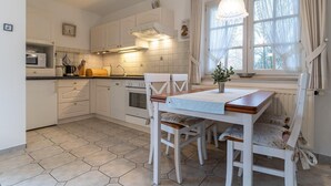 Een keuken met witte kasten, een houten tafel en een raam met gordijnen.