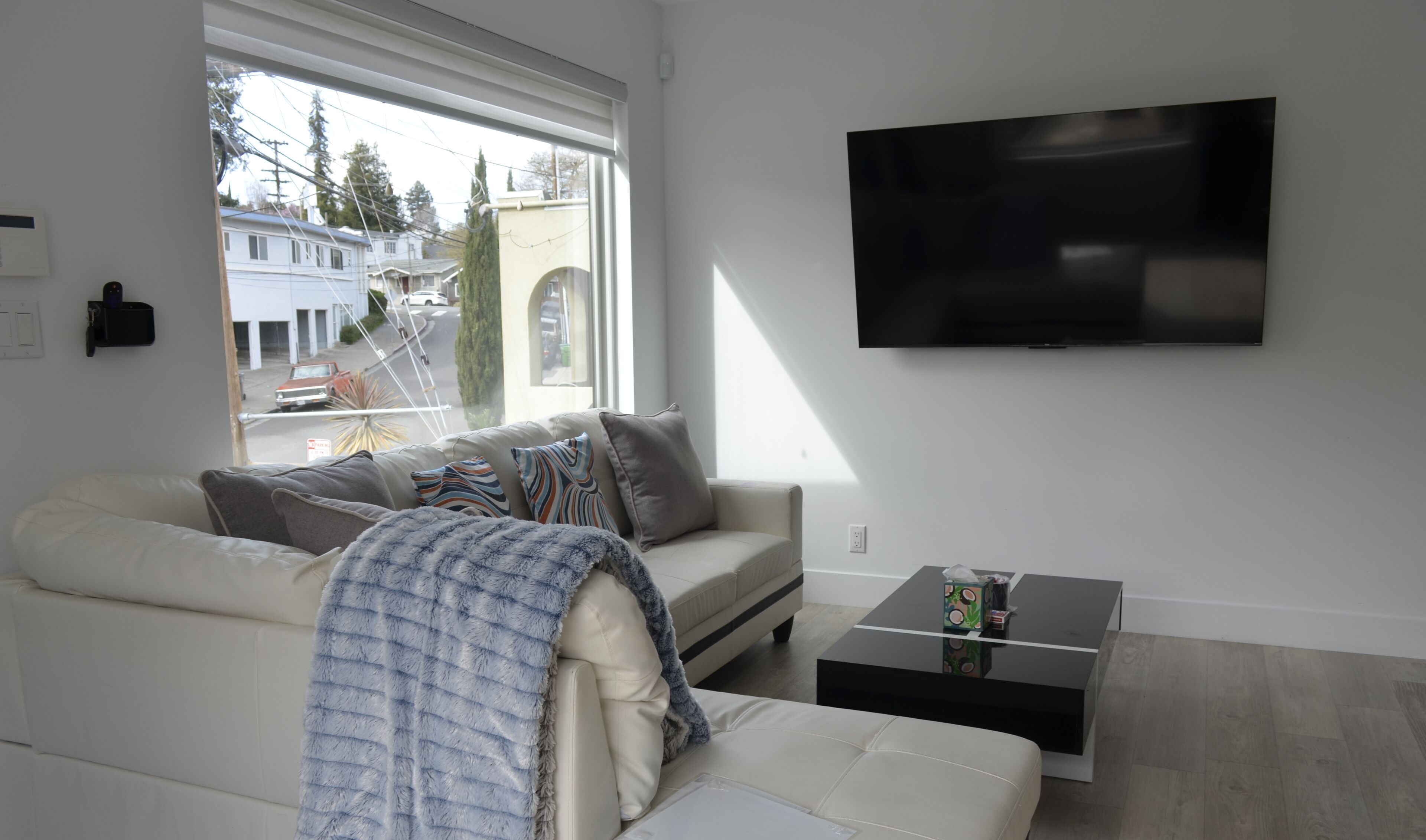A modern living room with a white sofa, a coffee table, and a flat-screen TV mounted on the wall.