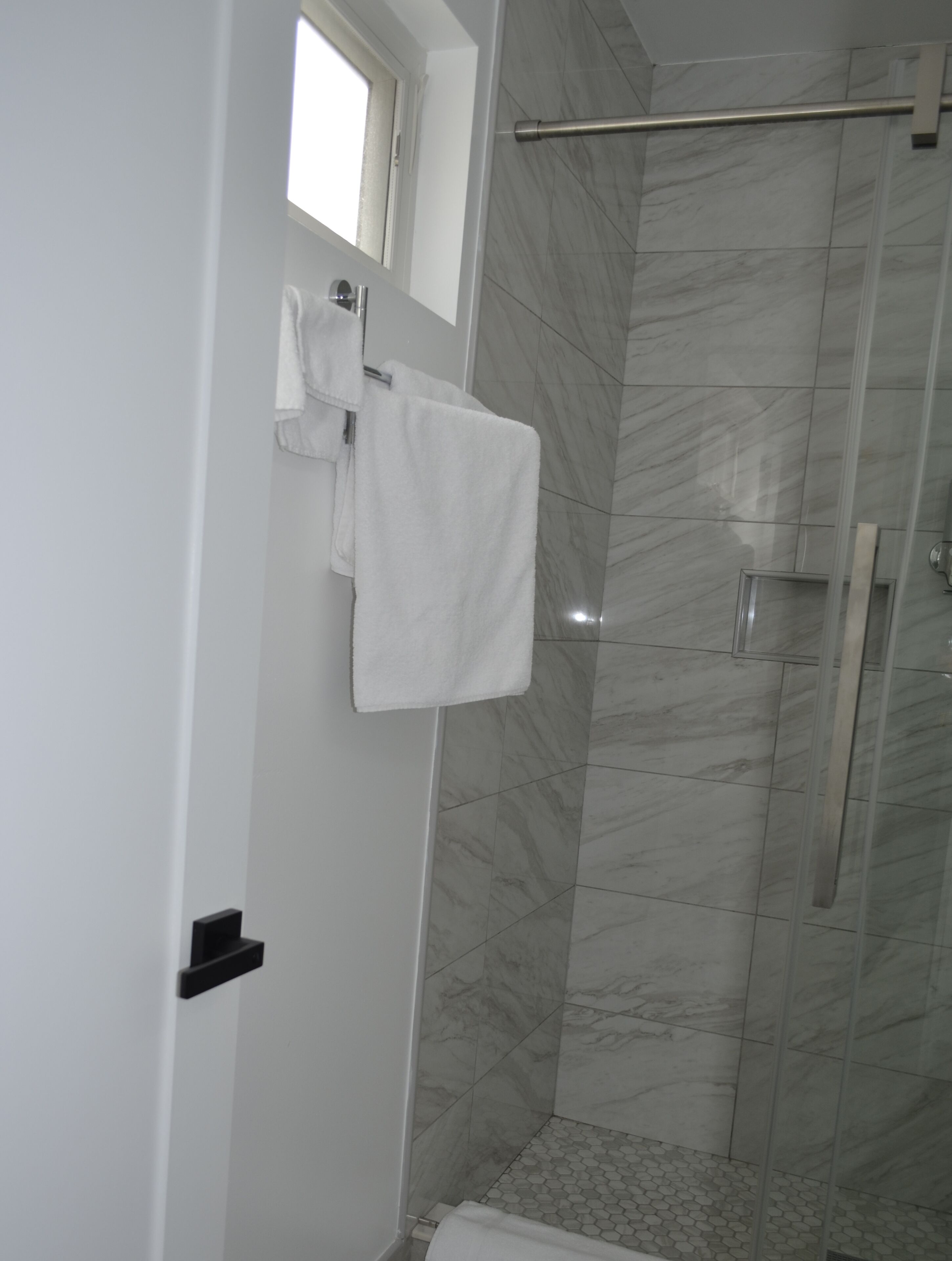 A bathroom with a shower, a towel rack, and a window.