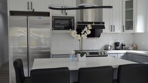 Egy modern konyha rozsdamentes acélból készült berendezésekkel, fehér étkezőasztallal és hozzáillő székekkel, valamint egy díszes, központi elhelyezésű orchidea-kompozícióval.
