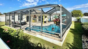 Una piscina coberta a l'exterior amb una estructura de vidre, envoltada per un jardí ben cuidat i una casa al fons.