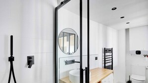 A modern bathroom with a glass shower enclosure, a round mirror, a wooden vanity, a toilet, and a washing machine. - Charming studio A/C - 2P - Le Marais (Paris)