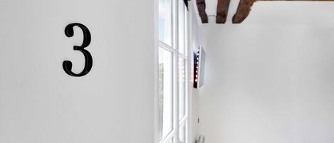 A room with a large number '3' on the wall, a window with blinds, and a small table with a vase of flowers.