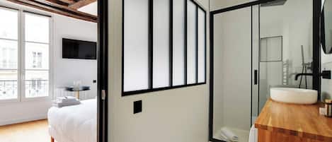 A modern bedroom with a large window, a wooden ceiling, and a bathroom with a glass shower and a wooden vanity.